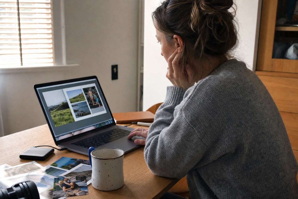 A person at a home desk designing a photo book on a laptop
