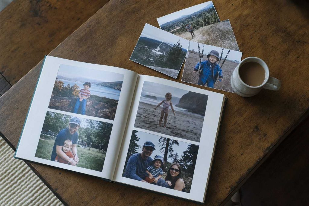 An open printed photo book on a wooden table with a few loose prints beside it